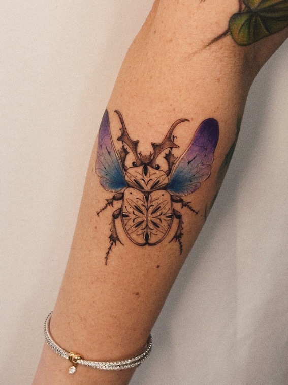 Tatuagem fine line de besouro colorido no braço